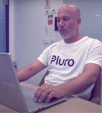 Shlomi, Pluro's Co-Founder and CTO, wearing a Pluro t-shirt, focused while working on a laptop in an office setting