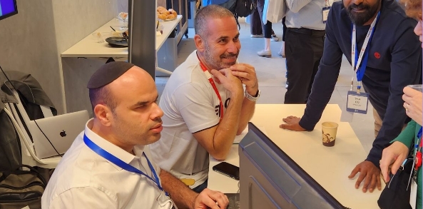 A group of people engaged in a discussion at a networking event, with Oren, Pluro's CMO, and Raffi Pluro's consultant seated at a table and others standing around