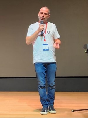 Oren, Pluro's CMO wearing a Pluro t-shirt and jeans, holding a microphone while presenting on stage