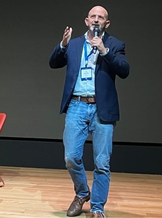 Ziv Tirosh Pluro's Co-Founder and CEO, on stage holding a microphone, wearing a dark blazer and jeans, delivering a presentation